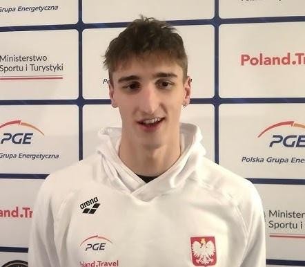 Ksawery Masiuk podczas wyścigu stylem grzbietowym, dynamiczne ujęcie z rozpryskującą się wodą, podkreślające jego technikę i siłę.