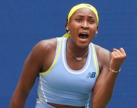Coco Gauff z zaciśniętą pięścią na korcie tenisowym, celebrująca zwycięstwo, z rozentuzjazmowanym tłumem w tle.
