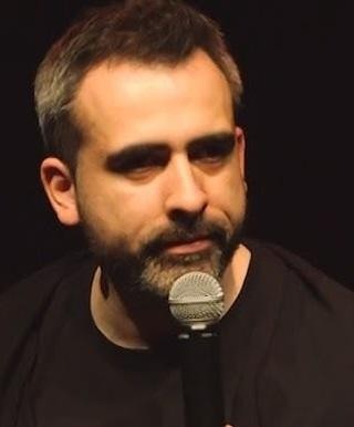 Abelard Giza podczas występu stand-upowego na scenie, w dynamicznej pozie, z mikrofonem w dłoni.