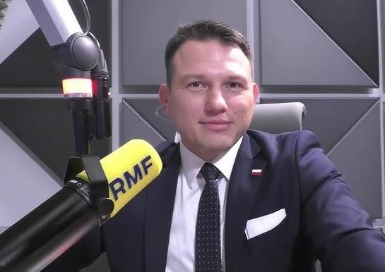 Sławomir Mentzen podczas wiecu wyborczego, przemawiający do zgromadzonych zwolenników, z widocznymi transparentami w tle.