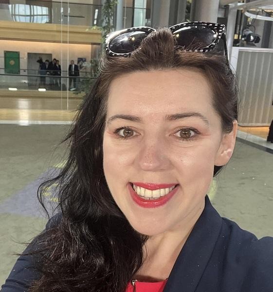 Dominika Ćosić w kontekście pracy dziennikarskiej, z elementami sugerującymi politykę międzynarodową lub instytucje UE w tle.