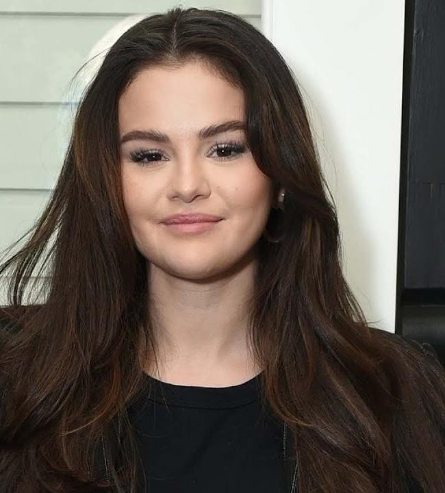 Selena Gomez podczas występu na scenie, śpiewająca z mikrofonem, w otoczeniu dynamicznego oświetlenia koncertowego.