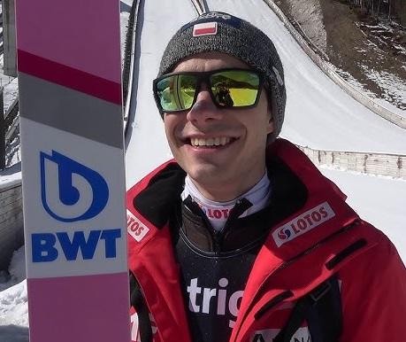 Jakub Wolny podczas treningu skoków narciarskich, skupiony na technice, na tle skoczni.
